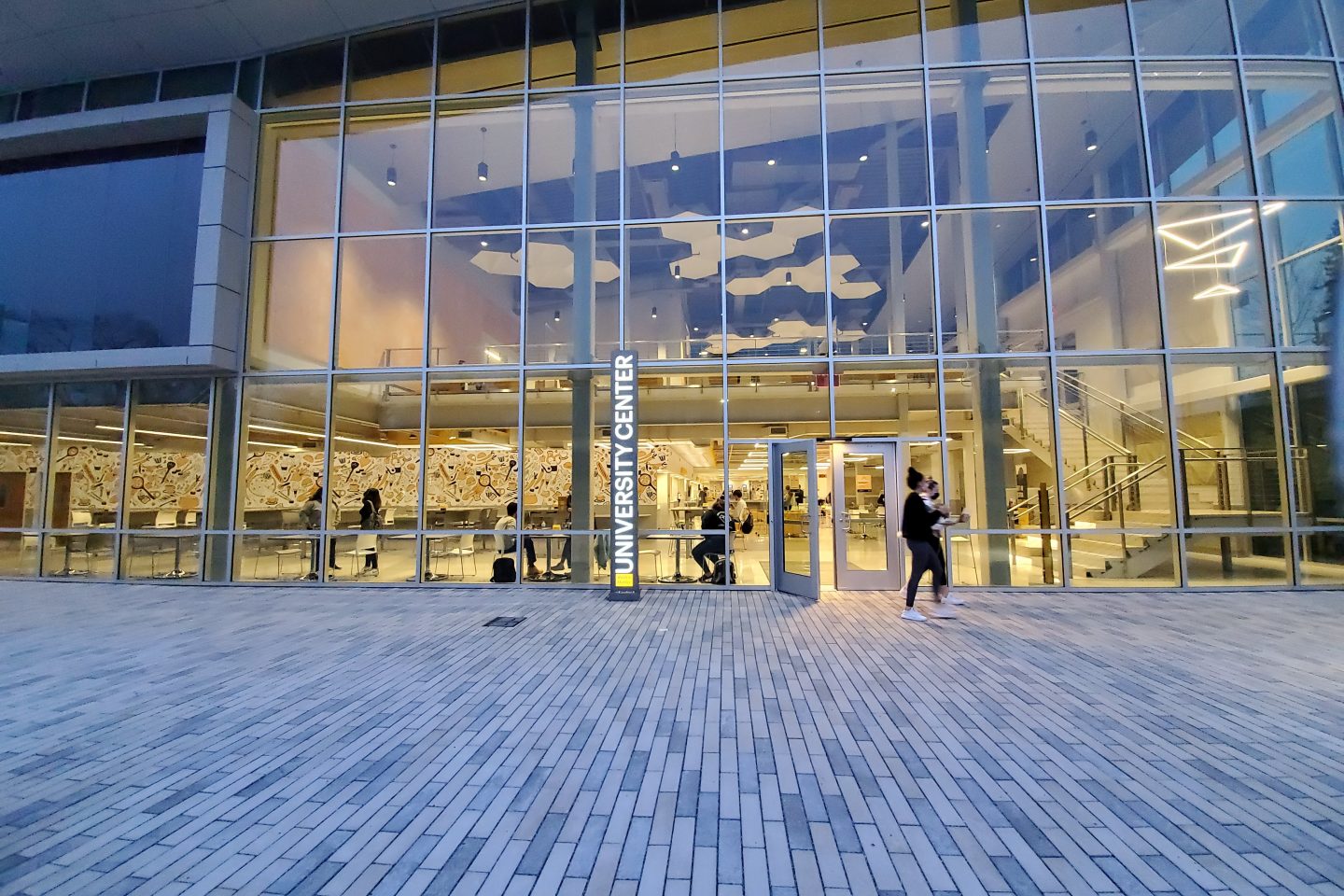 The all-glass front entrance of the Ruth S. Harley University Center, shown at night with the interior lobby illuminated from floor to ceiling