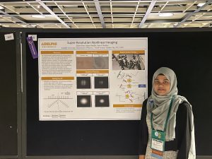 Zahin Ritee standing in front of a research poster for her research in physics.