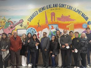 A group of people stand in front of a mural that reads "Shaheed Hemu Kalani Govt. S.B.V. Lajpat Nagar"