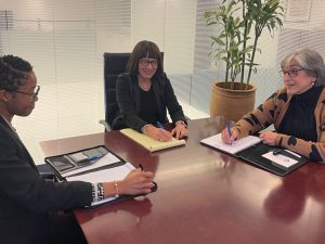  A young Black woman and two older white women at an office table