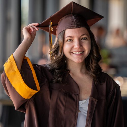 A young woman in Adelphi University graduation attire smiles confidently.
