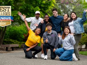 A joyful group of students walking on Adelphi's campus surrounded by trees and greenery