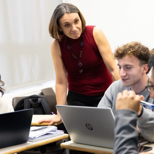 Adelphi University professor interacting with smiling students in a classroom setting.