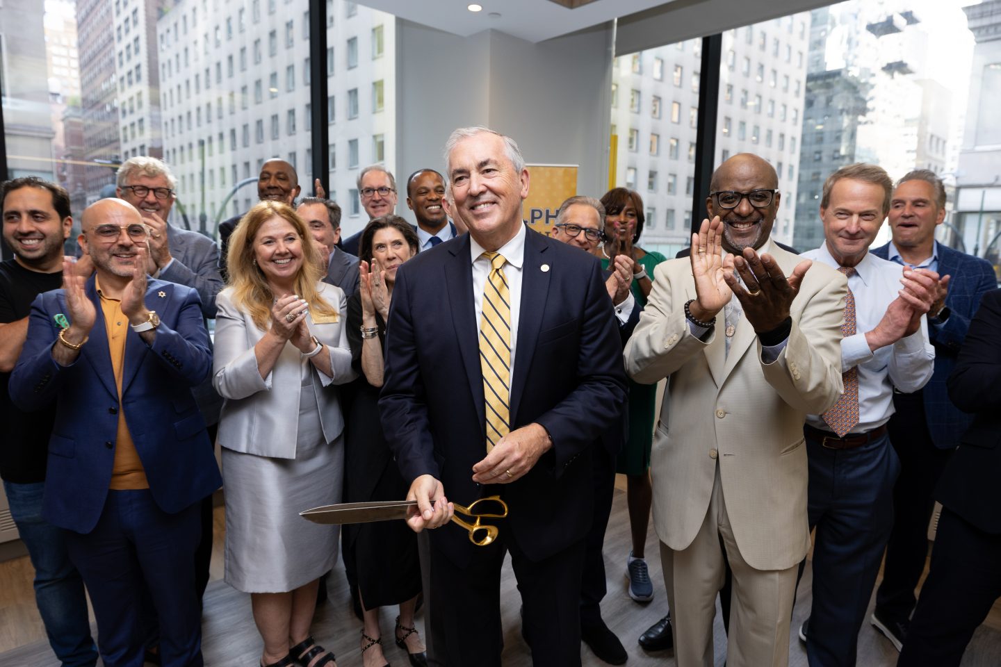 President Balboni cuts the ribbon with members of the Board and Executive Leadership cheering him on.