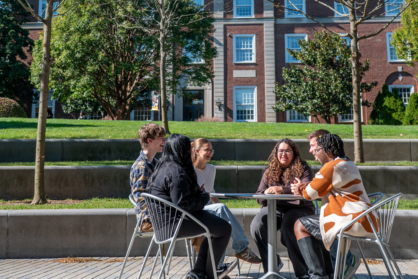 Students sit at a table on the patio outside the Ruth S. Harley University Center, with Levermore Hall in the background.