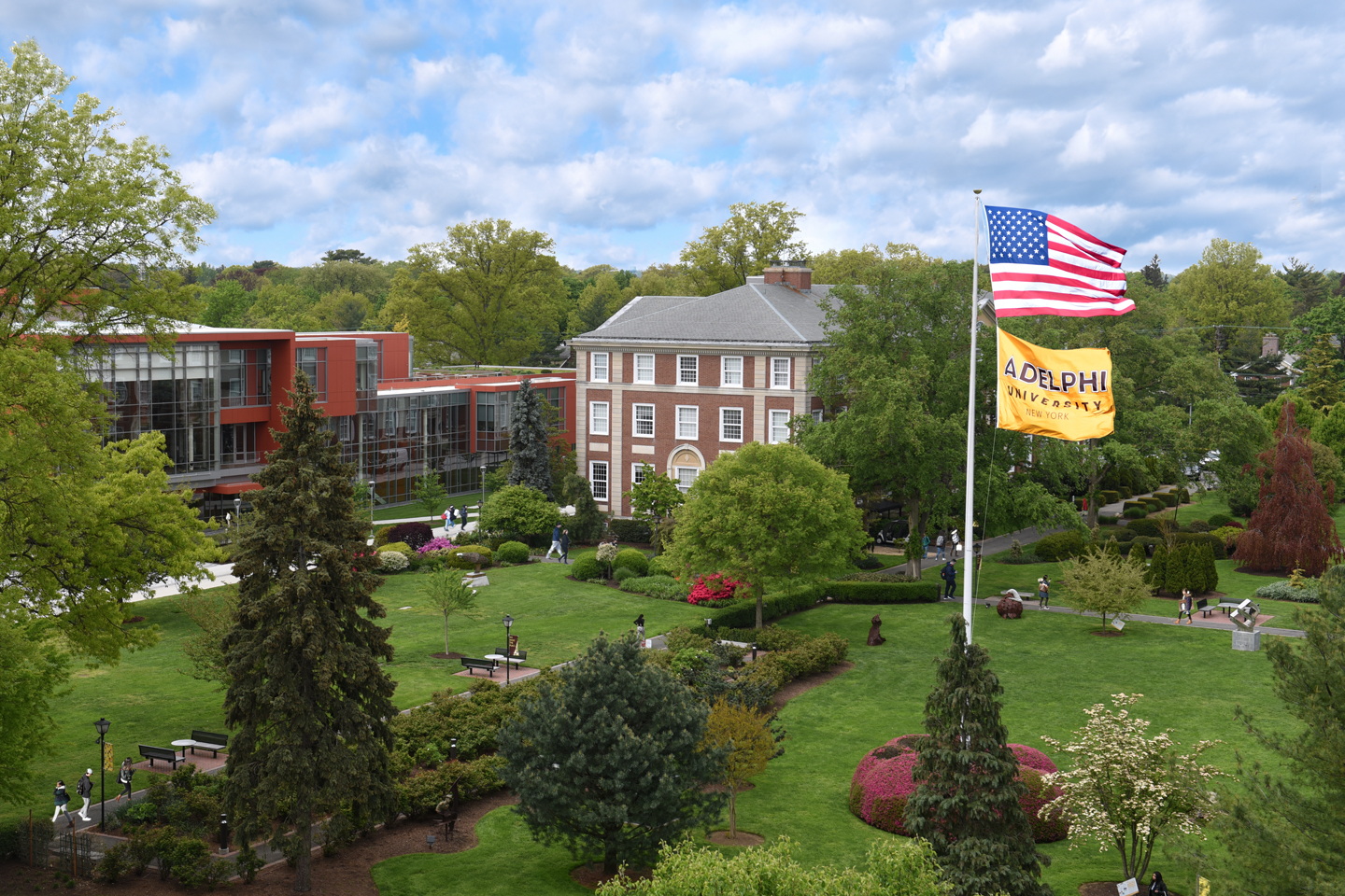 A shot of campus in summer, with the lawns in front of the two buildings and the American flag and Adelphi flag at right.