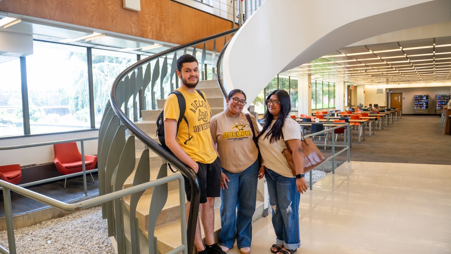 Adelphi students standing in Swirbul Library by the staircase.