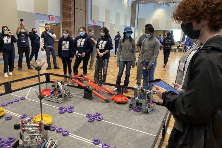high school students at a robotics event working with the robots.