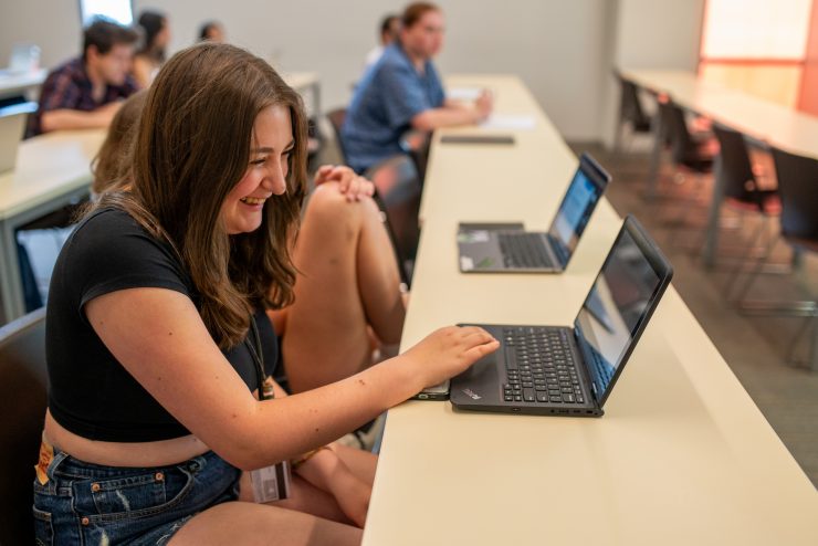 Happy Adelphi student laughing while casually working on her laptop in class.
