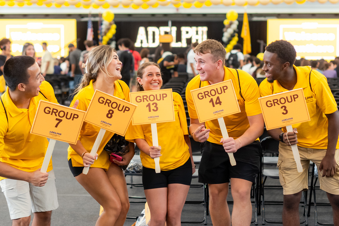 Five smiling PALs wearing identical gold shirts, each holding a small sign identifying the numbered group they are leading
