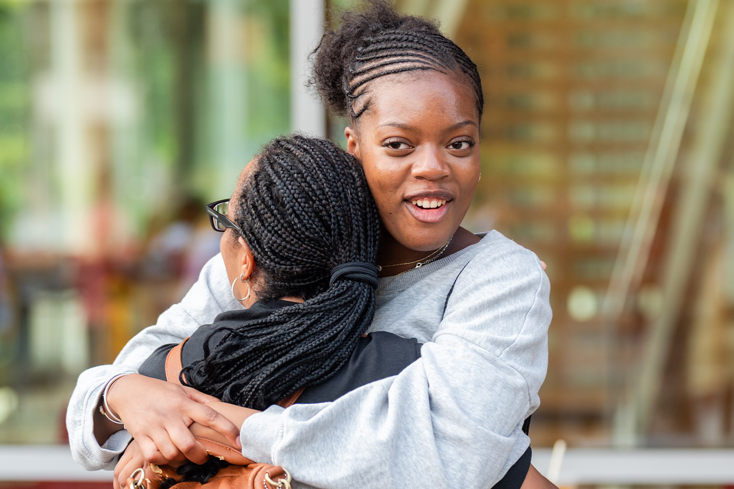 A student faces the camera as she hugs her mother, whose back is turned to the camera.