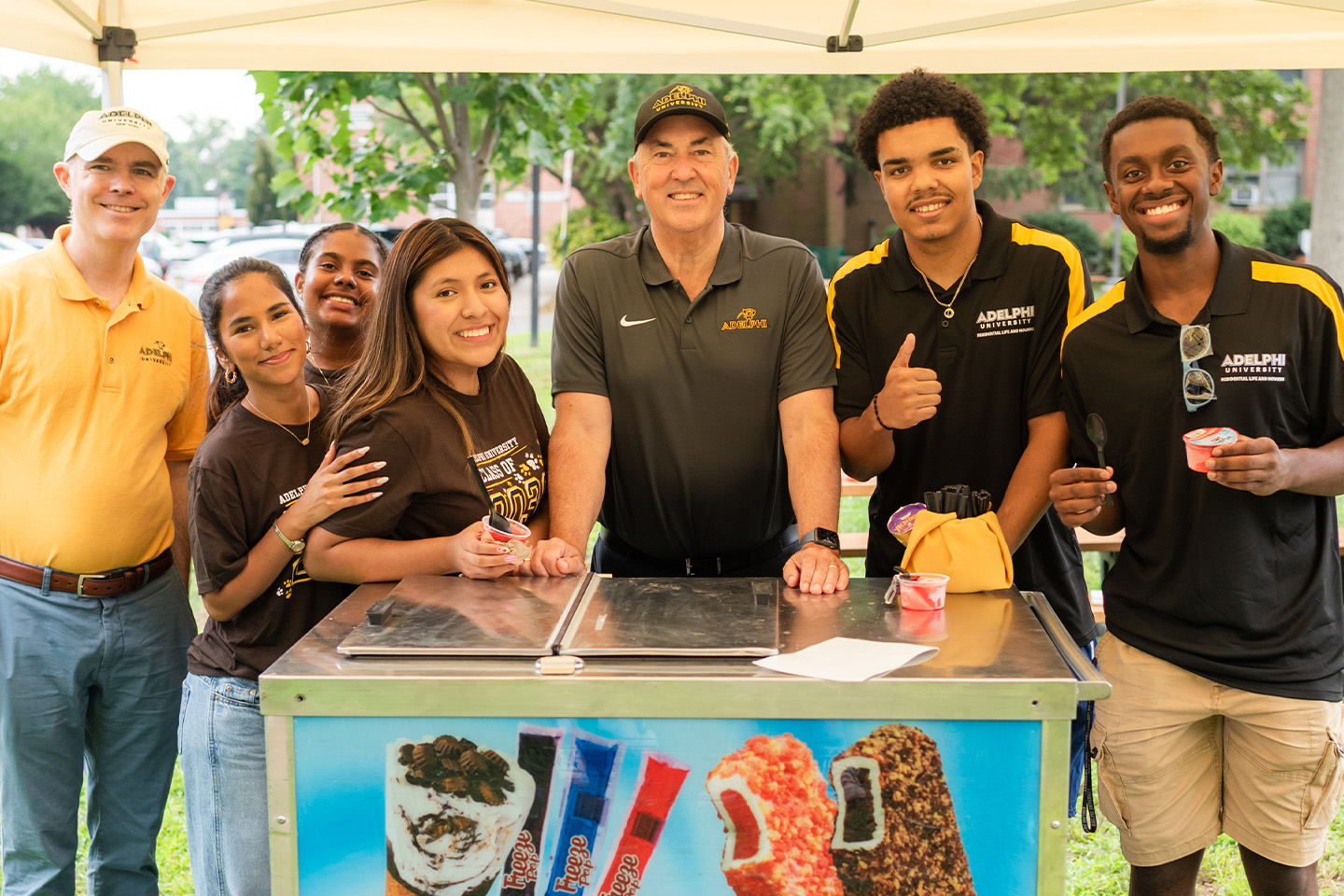 The two Adelphi leaders pose with the students while standing behind an ice cream cart.
