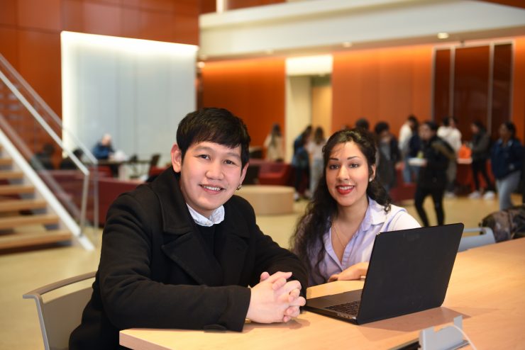 Male and female Adelphi students together in the Nexus Building lobby on a laptop.