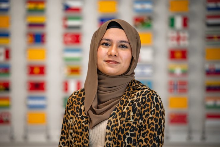 An Adelphi international student stands in the Ruth S. Harley University Center in front of the wall of international flags.