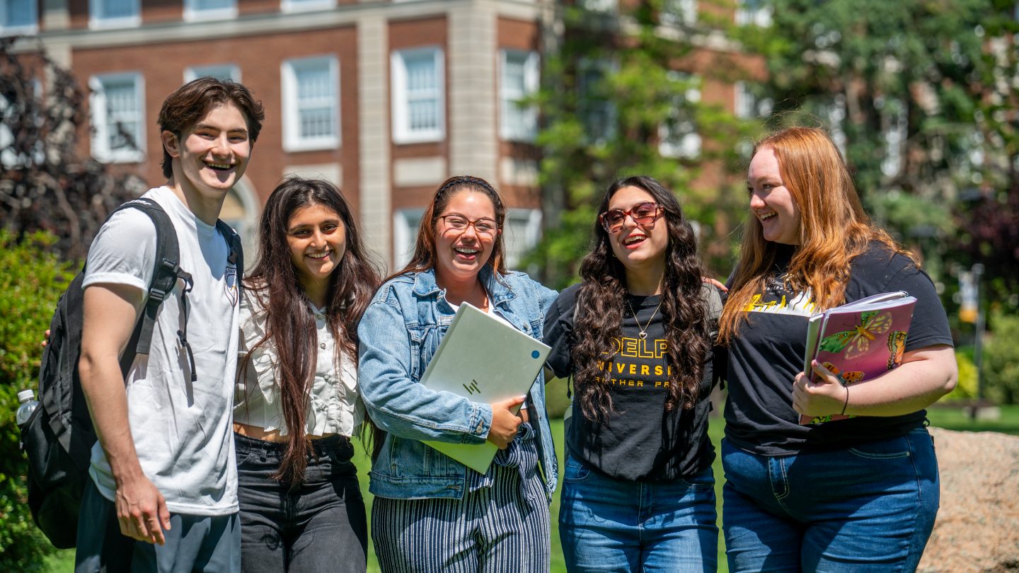 A group of Adelphi University students standing in front of Levermore Hall on campus.