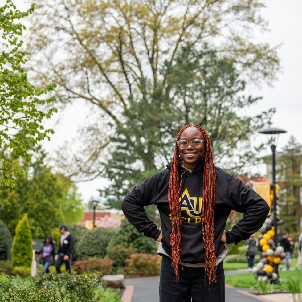 Adelphi student stands confidently wearing an AU sweatshirt on on Adelphi University's Garden City campus.