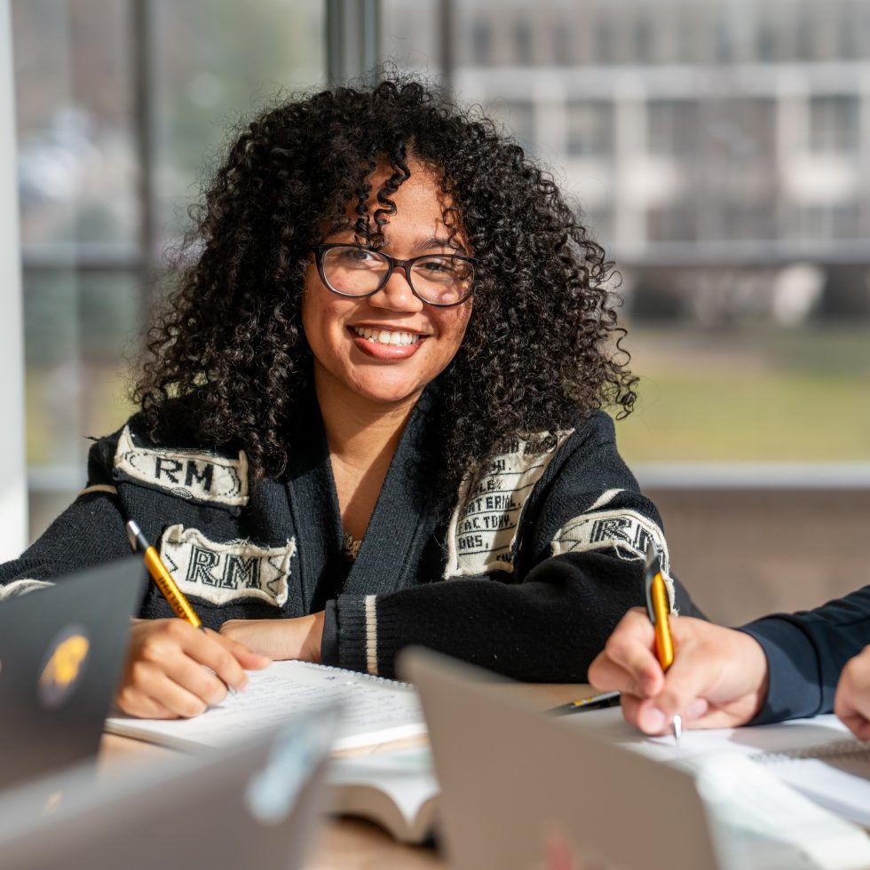 Student smiles at table with laptop studying at Adelphi
