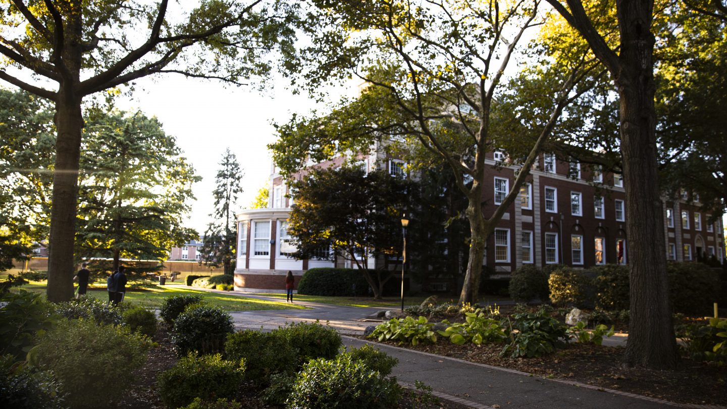 Blodgett Hall peeking through sun-dappled trees on Adelphi University's campus.