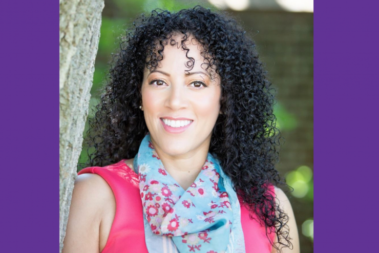 A woman with curly hair, smiling, wearing a black blazer 