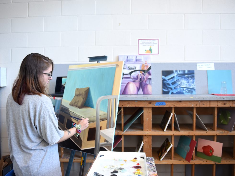 A studio art student works on an oil painting in the Fine Arts studio on campus.