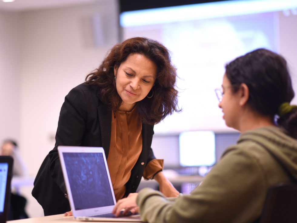 Professor Ines Archer leads over to see a student's laptop screen during class. Engaged learning.
