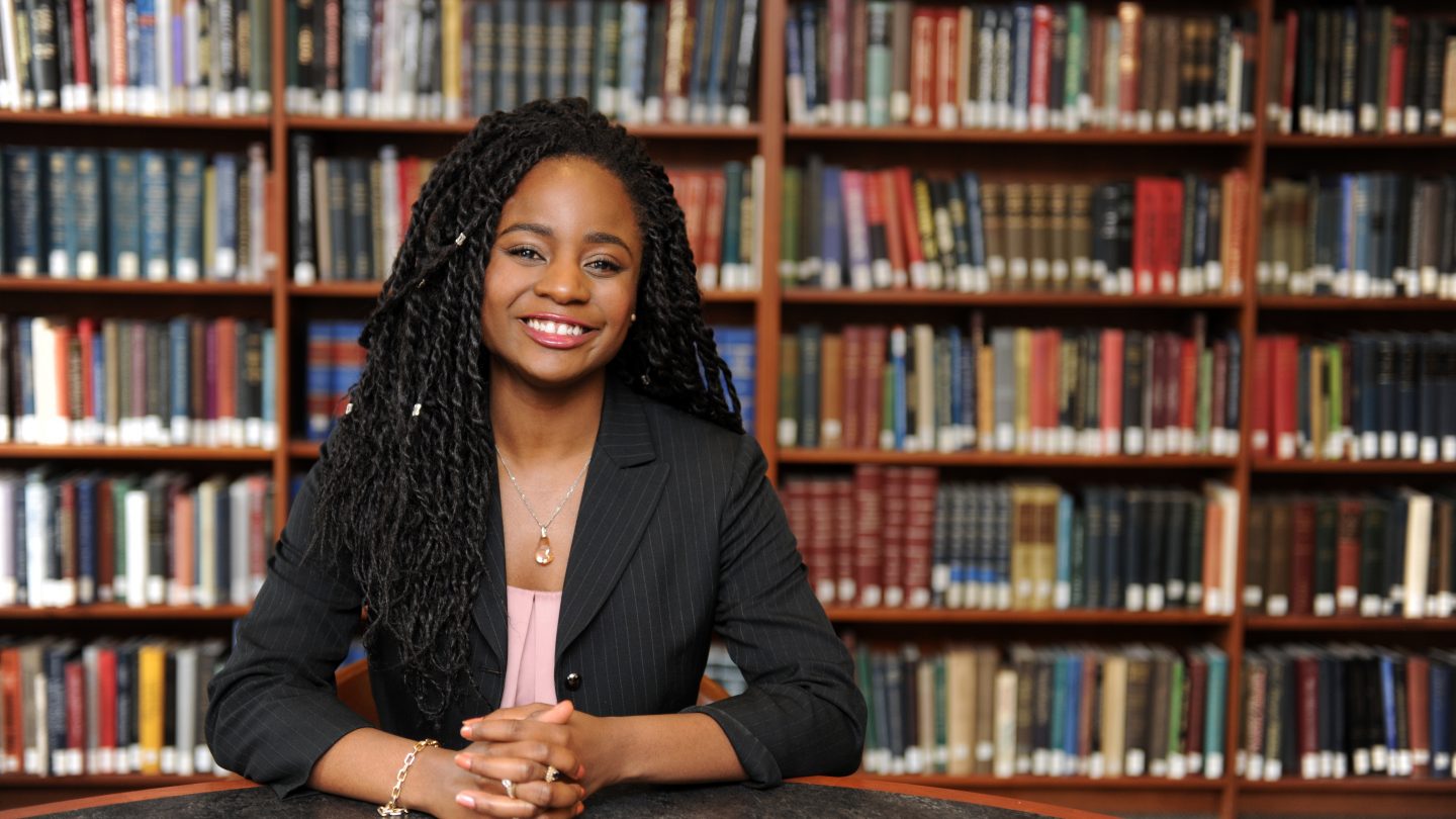 Adelphi alumnae TaLona Holbert pictured at a table with law books in the background.