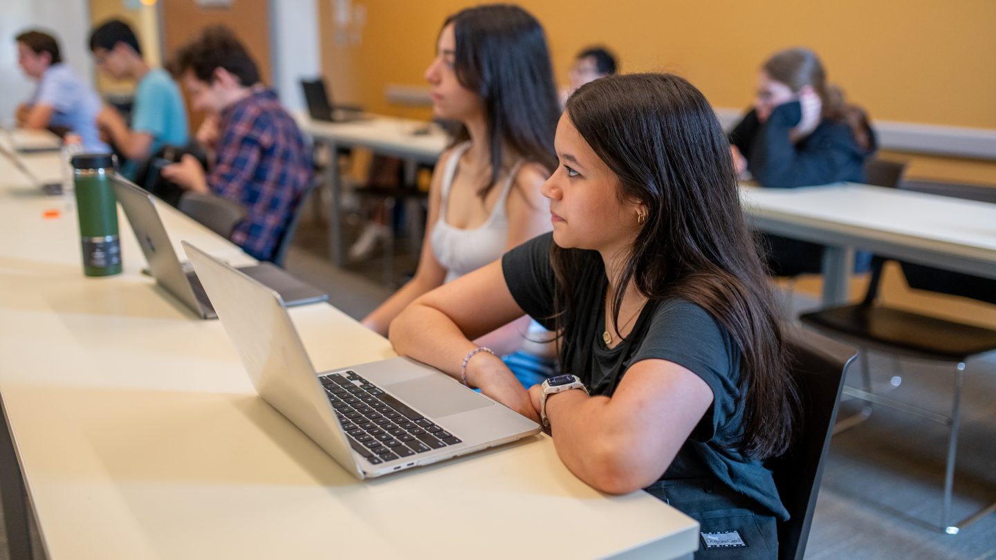 A student in Adelphi’s pre-college Communication and Critical Thinking course listens to a lecture with a laptop open in class.