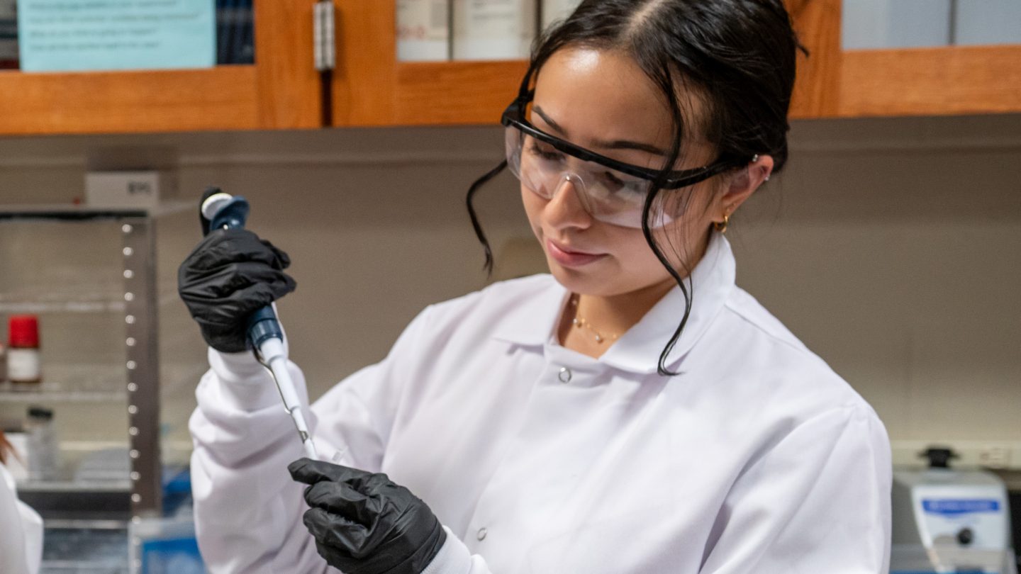 female student in a whit lab coat working in the Adelphi University chemistry lab