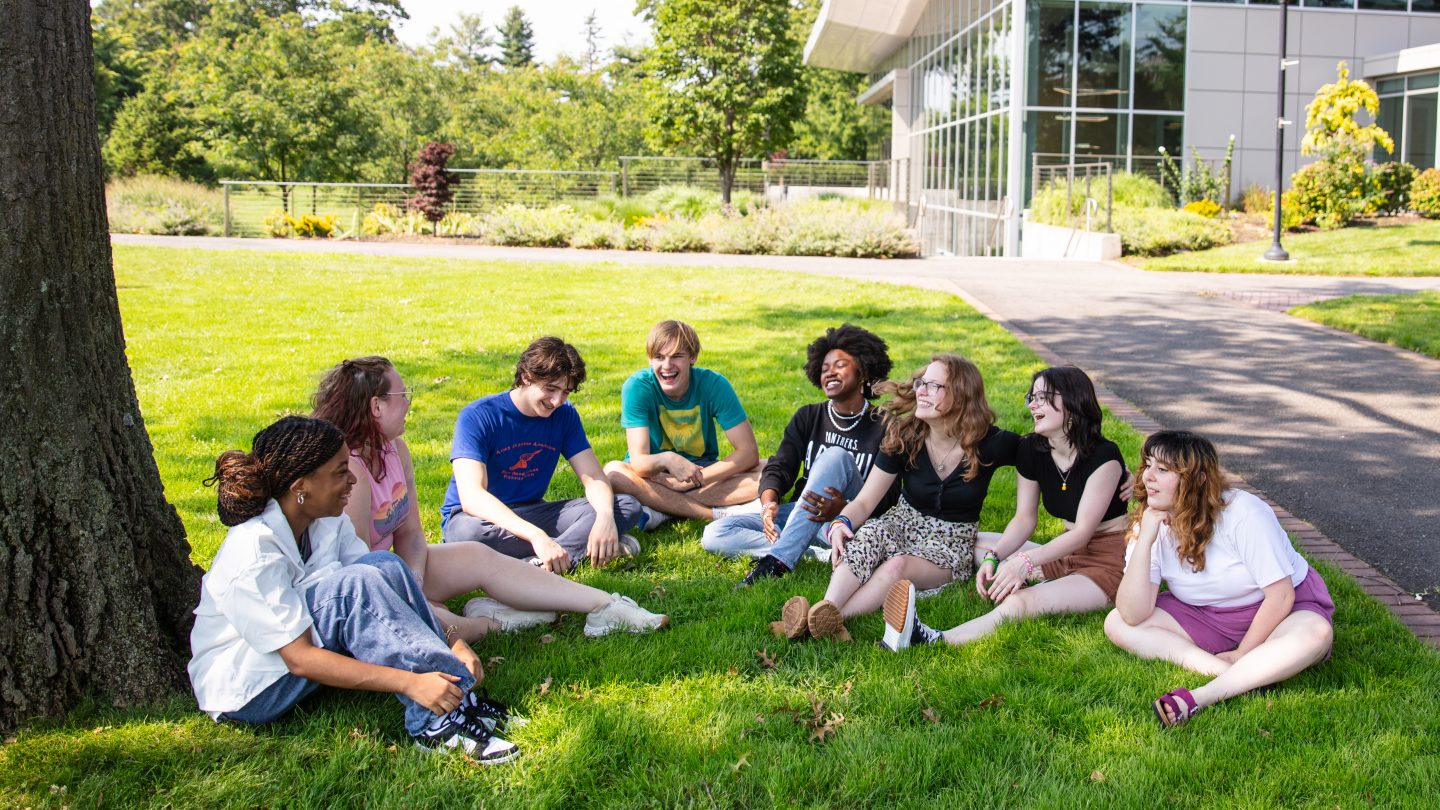 High school students sitting in a circle on the lawn at Adelphi University's campus.