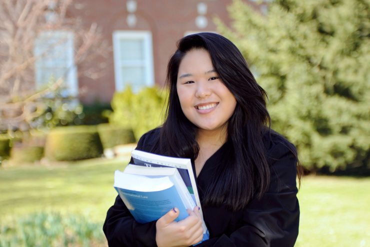 Female Adelphi student holding law books on campus.