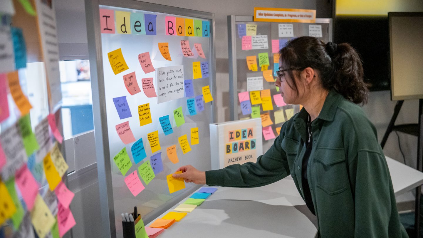 Student placing post-it on the wall in the innovation center at Adelphi.
