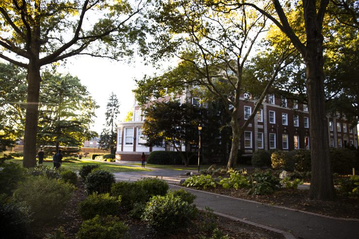 Blodgett Hall peeking through sun-dappled trees on Adelphi University's campus.