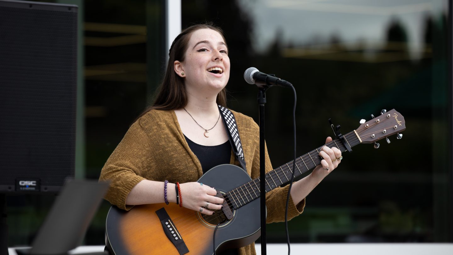 An Adelphi student sings while playing a guitar on campus.