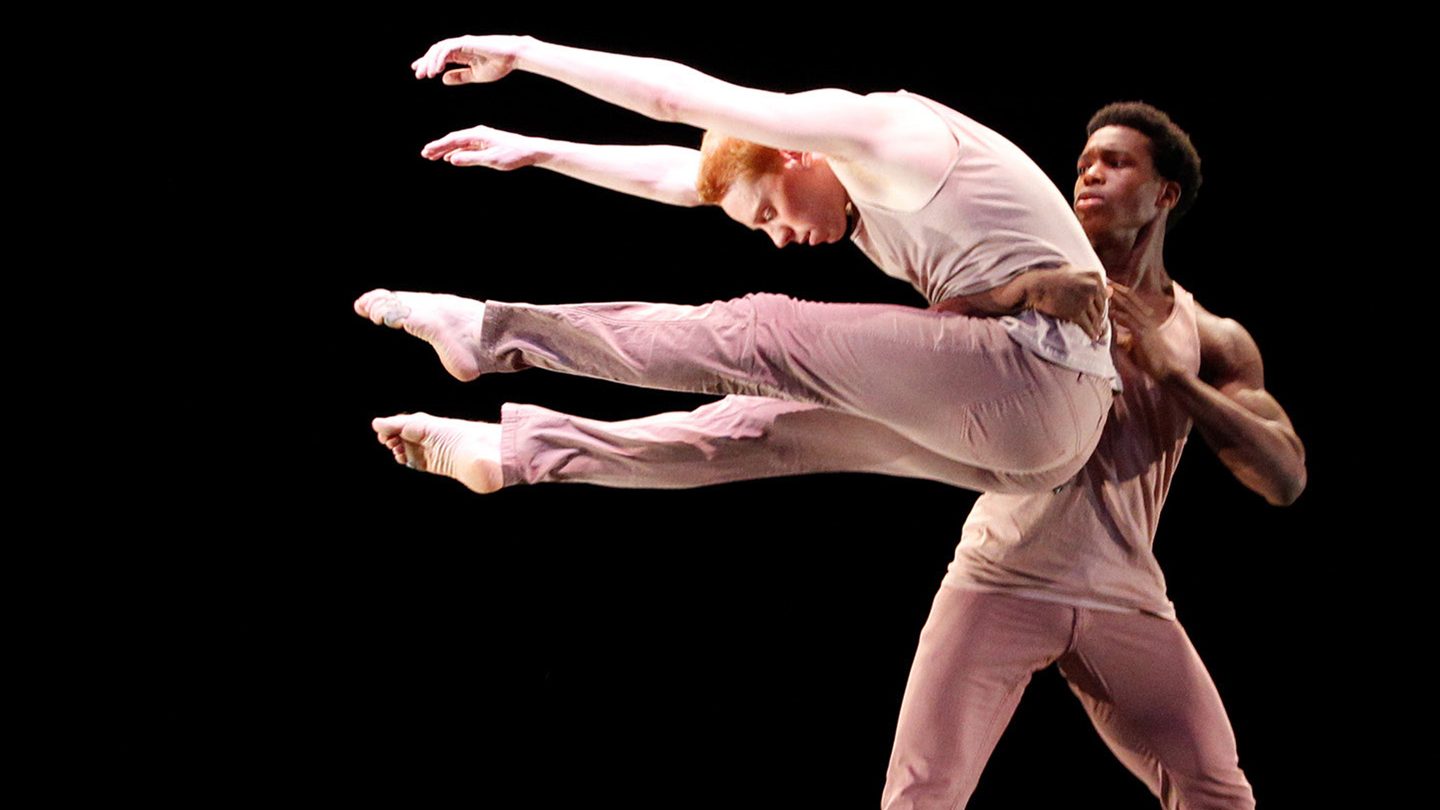 Two male Adelphi University dancers perform on stage.