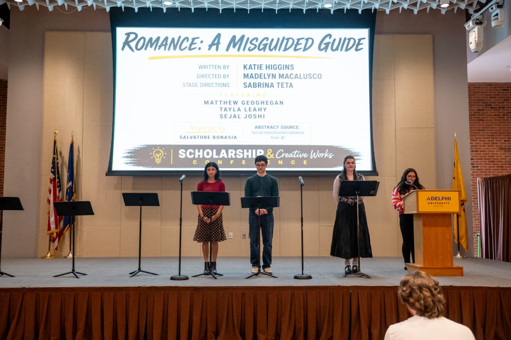 Four acting students on stage with a projection behind that states: "Romance: a Misguided Guide"