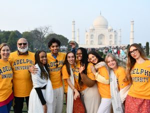 A group of students and faculty standing in front of the Taj Mahal in India wearing yellow Adelphi t-shirts