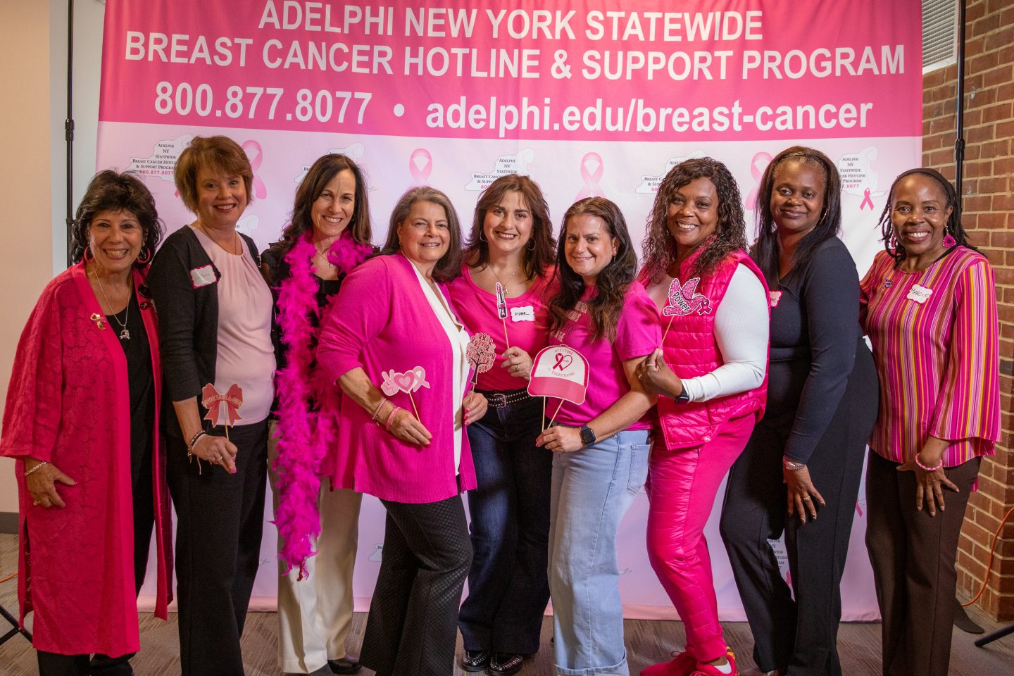 Nine women in front of a pink breast cancer hotline backdrop