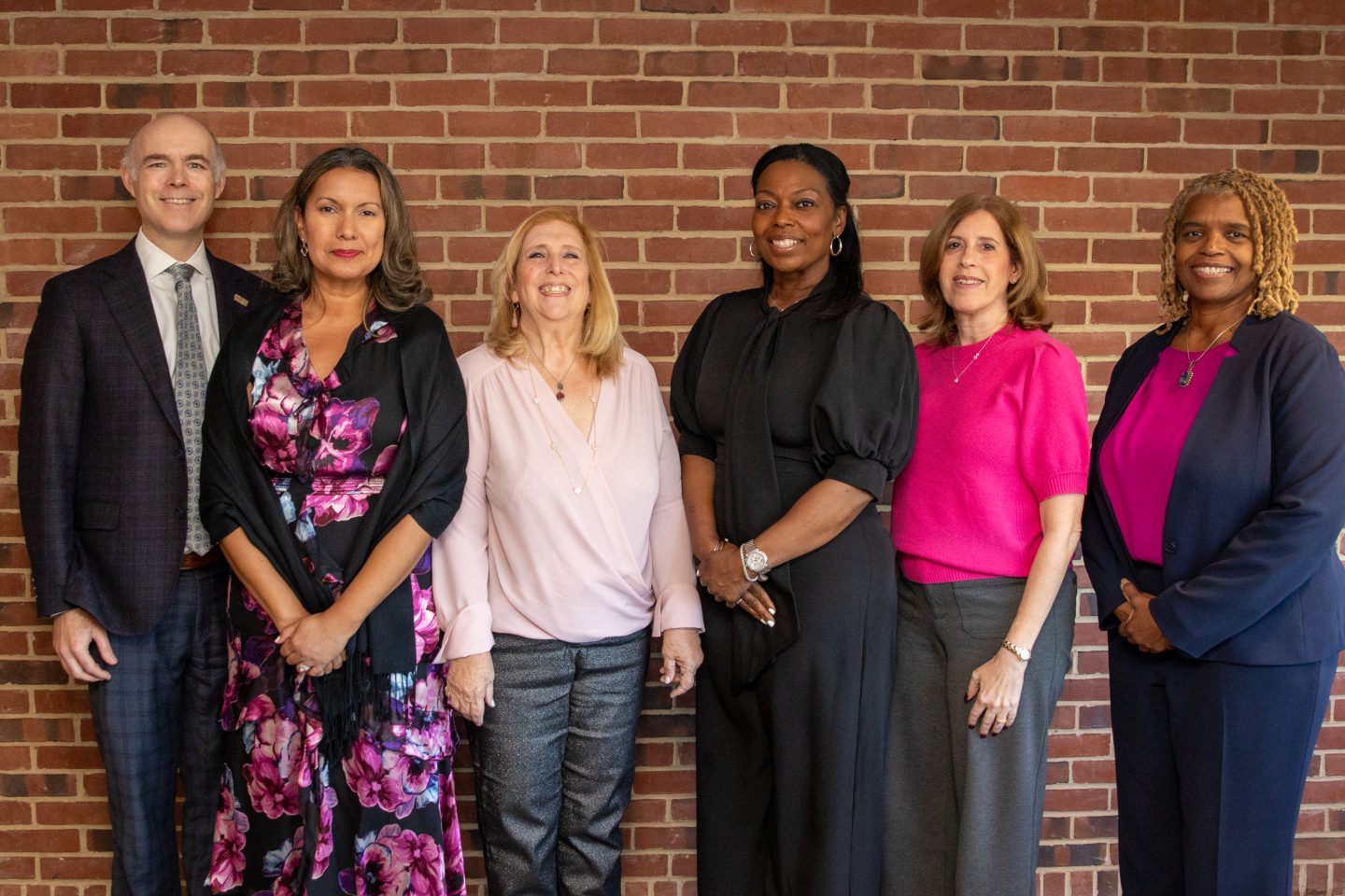 Five women and a man in front of a brick wall