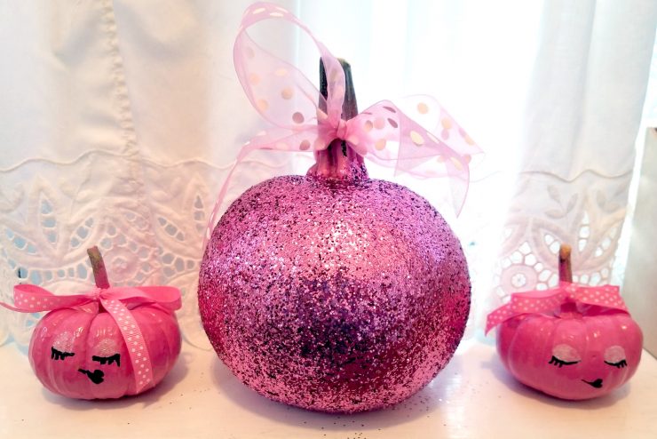 Pink painted pumpkins on a window sill. One is glittery.