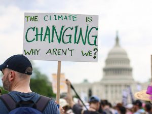 A man holding a sign that says "the climate is changing, why aren't we?"