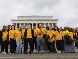 A group of about 25 students, faculty and administrators stand before the Lincoln Memorial.