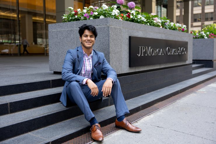 Adelphi student Monish Churaman sits in front of the JPMorgan Chase & Co sign in NYC, where he secured an internship.