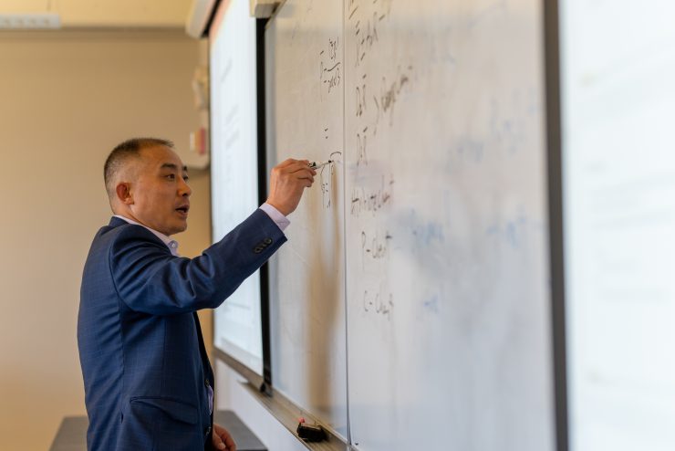 Jiang Zhang writing on a whiteboard during a Marketing class at Adelphi University