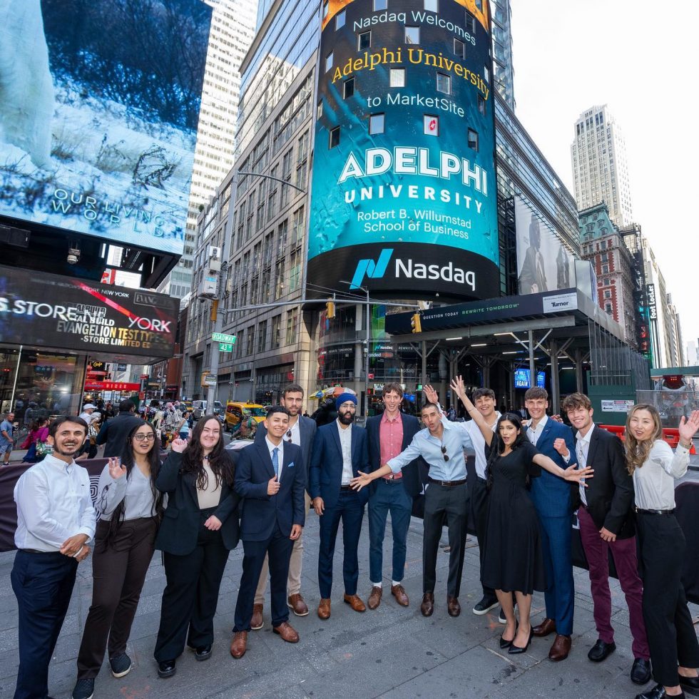 Adelphi students stand in Time Square in New York City in front of the Nasdaq with the Adelphi University Logo displayed on the large screen.