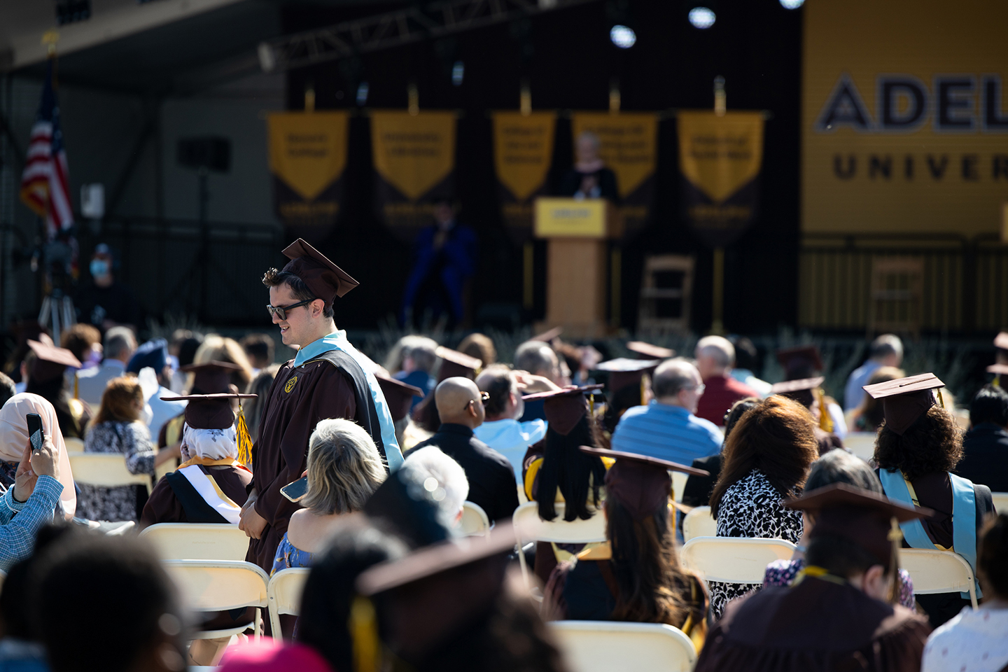 Graduate walking through seated audience with a view of the commencement stage in the background.