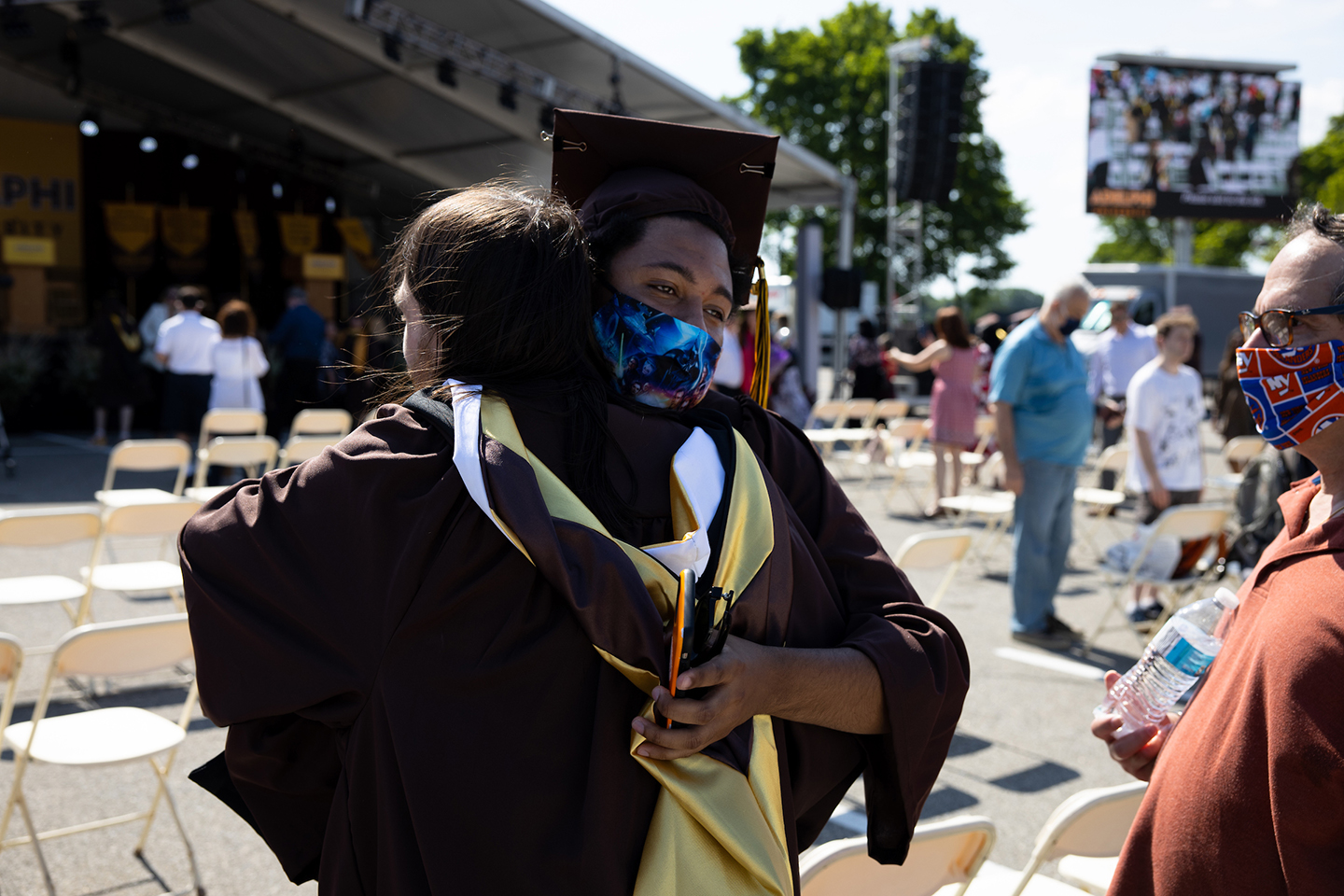 Two graduating students embrace while wearing masks.