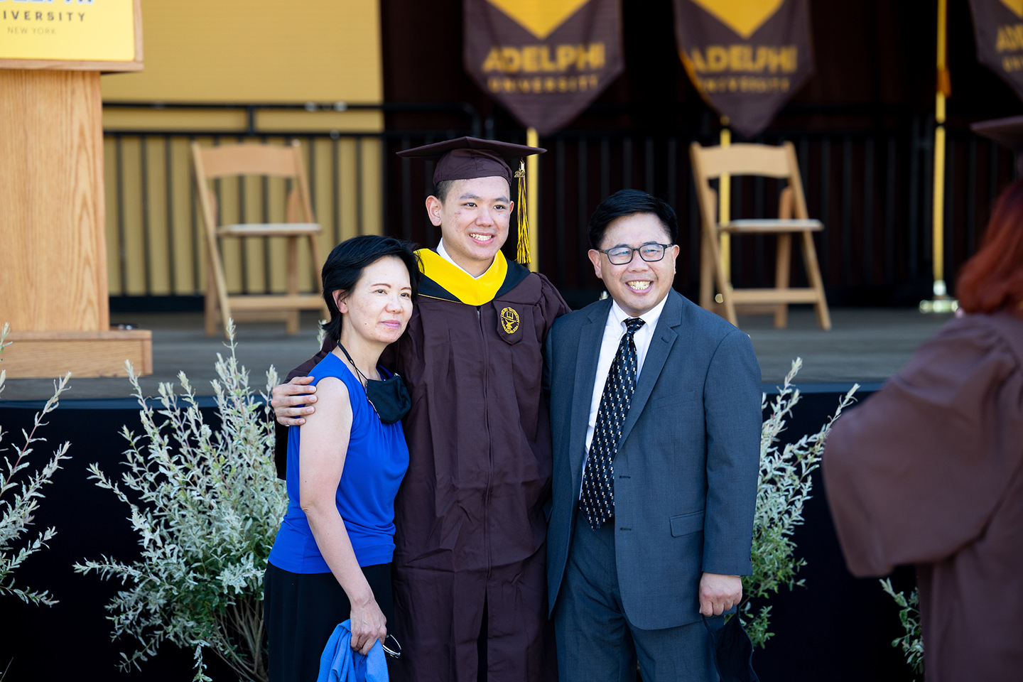 Graduating student poses with parents in front of commencement stage.