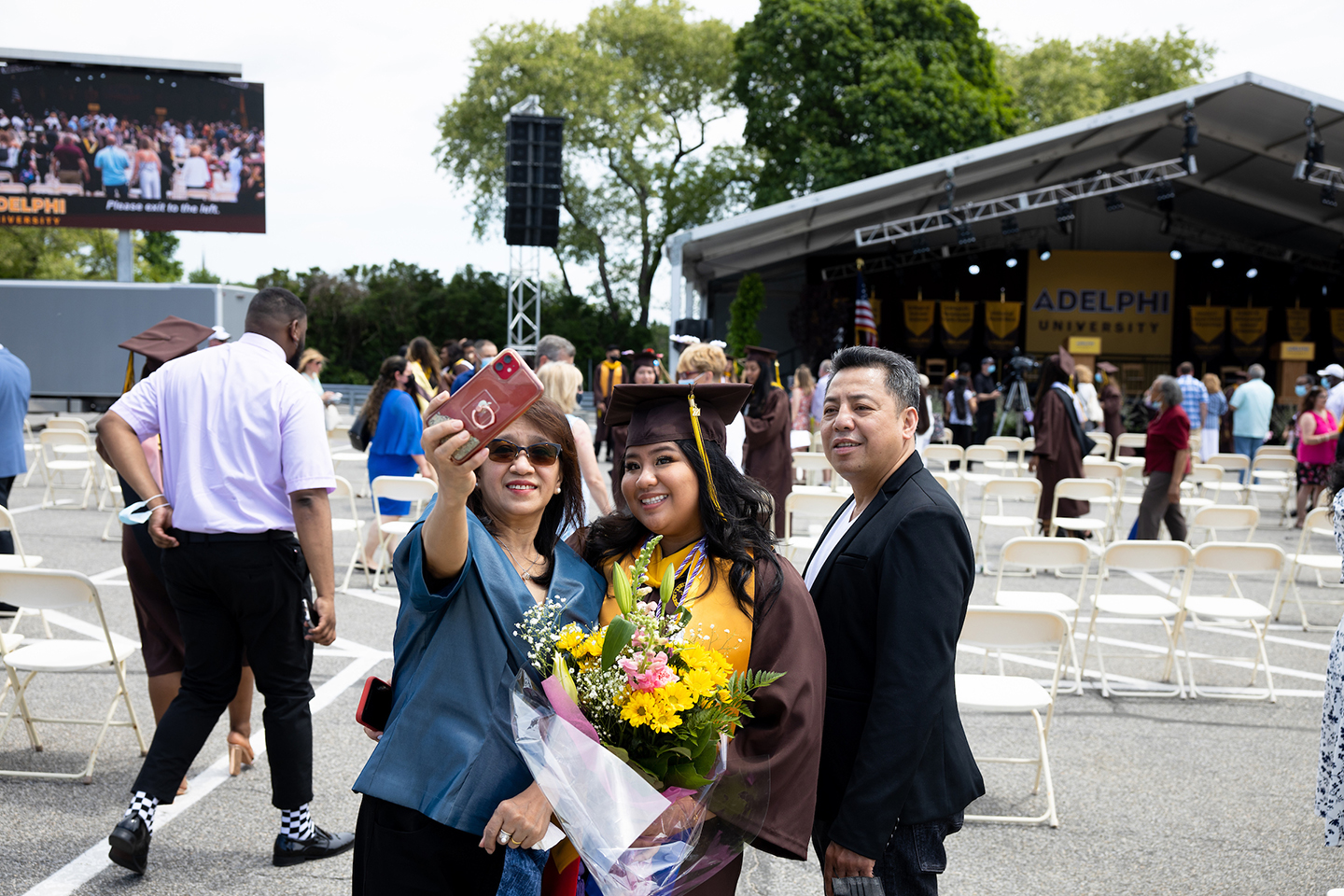 Graduate holding bouquet poses for picture with parents.