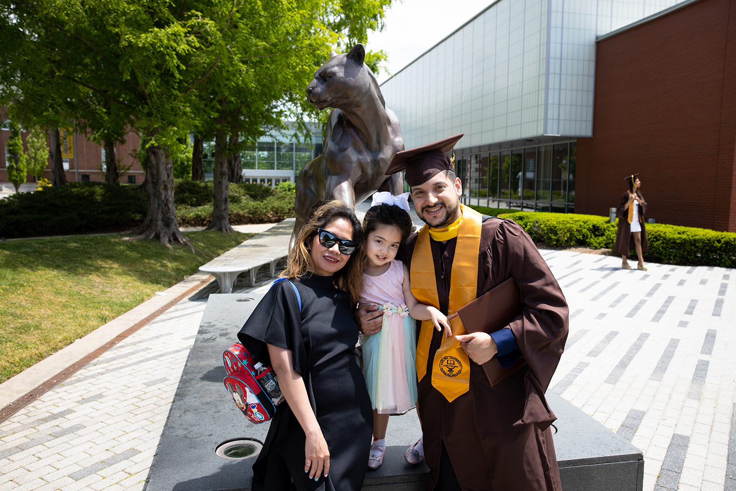 A graduate poses with his family in front of the Panther Statue on campus.