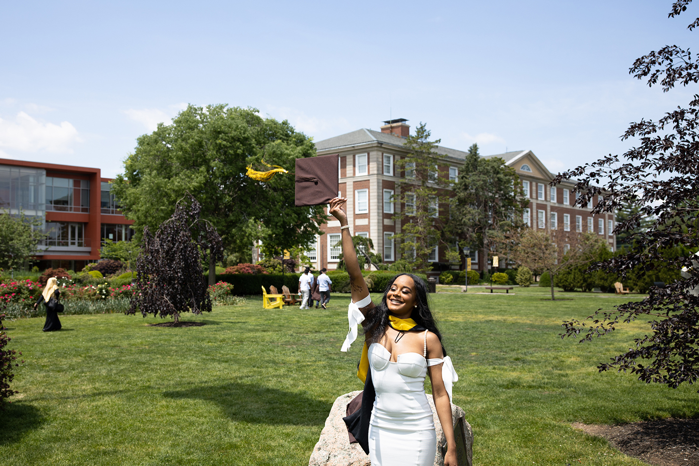 An Adelphi graduate throws her cap in front of Levermore Hall on campus.